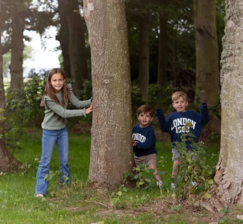 Children playing hide and seek behind a tree in a lush green park.