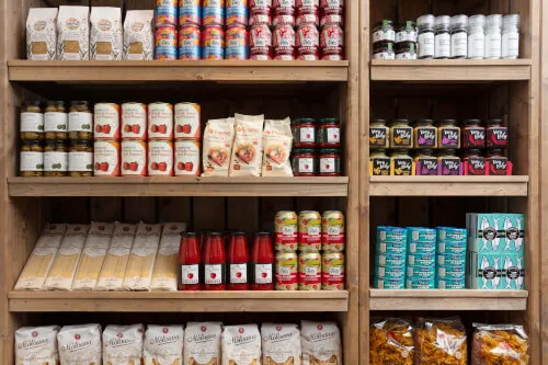 A shelf displaying various food products including canned goods, pasta, sauces, and snacks.