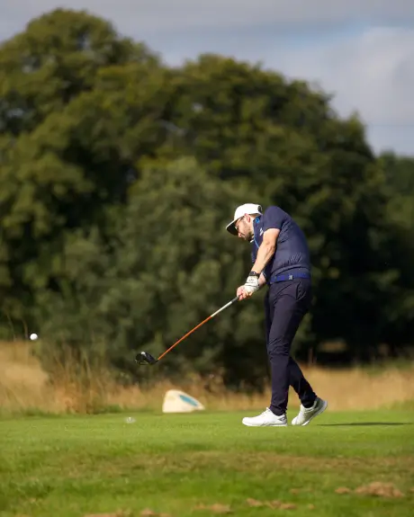 Golfer swinging a club at Roxburghe Golf Course, set in picturesque surroundings.