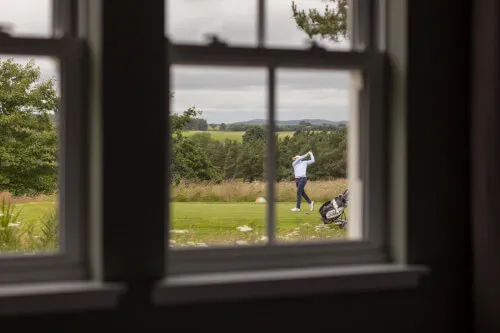 Golfer swinging on the course seen through window at Roxburghe Hotel Golf & Spa Ltd.