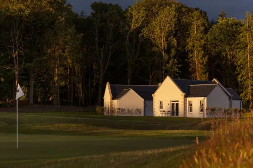 A picturesque view of Roxburghe Hotel Golf & Spa with a golf flag in the foreground and trees in the backdrop.