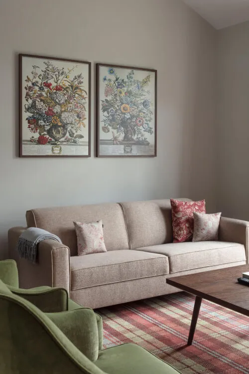 A modern living room with a brown sofa, floral paintings, and a green armchair at Roxburghe Hotel Golf & Spa.