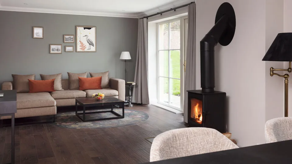 A cozy living room with a sofa, wood stove, and large windows.