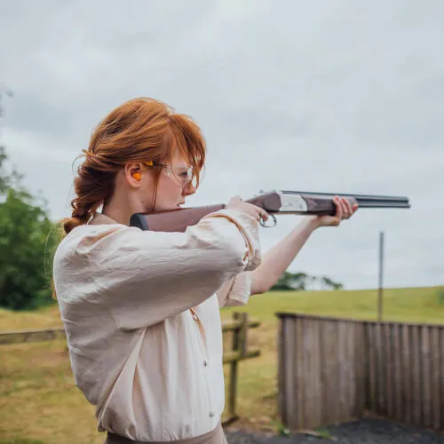 A woman aiming a shotgun at a shooting range.